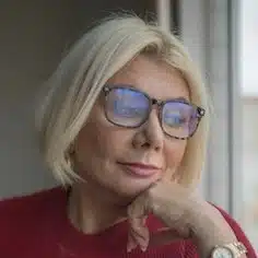 A woman with blonde hair and glasses is posing for the camera.