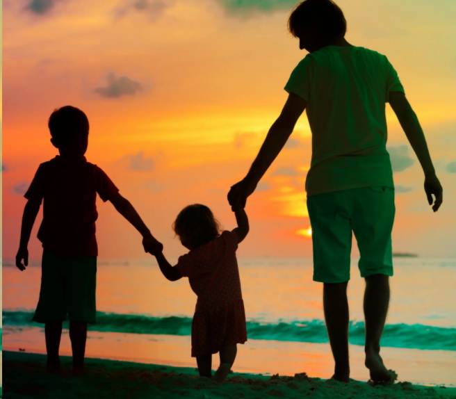 A man and two children holding hands on the beach.